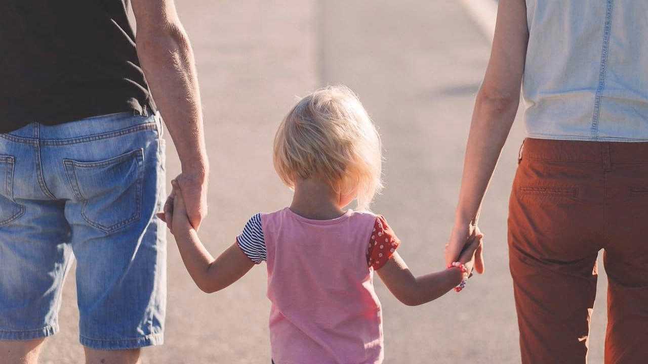 A parent and child walking together, holding hands, in warm evening light.